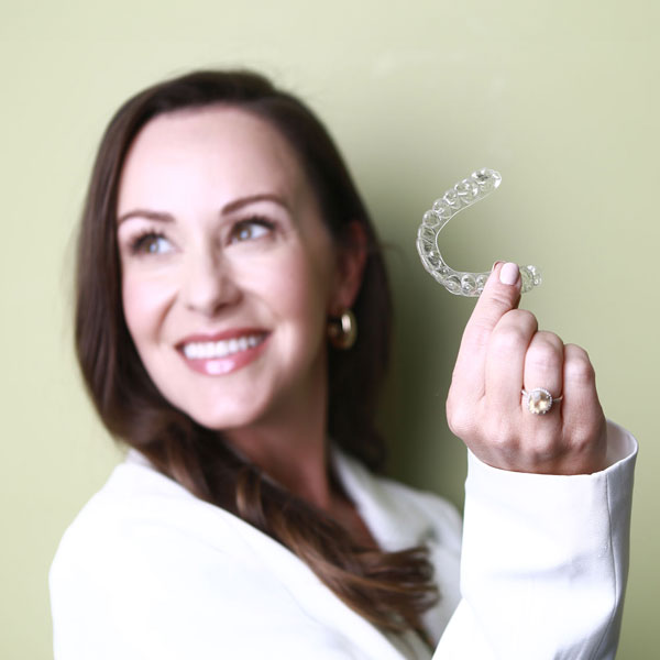 woman smiling and holding up clear aligner for teeth